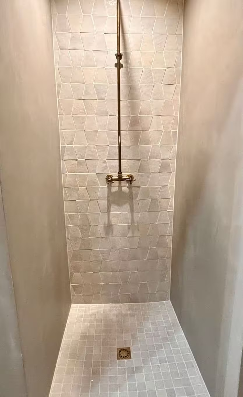 Douche italienne dont le mur de face est couvert d'un carrelage trapézoïdal de couleur clair donnant du relief à la pièce